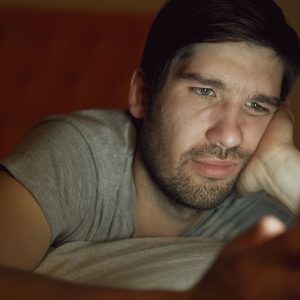Hombre en una habitación oscura mirando el móvil con preocupación por adicción a Internet.