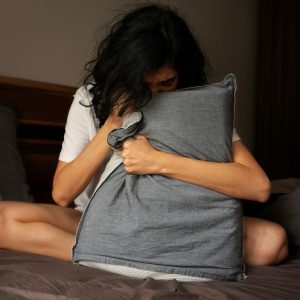 Mujer con ansiedad sentada en la cama abrazando un cojín durante el tratamiento de la ansiedad en Chiclana.